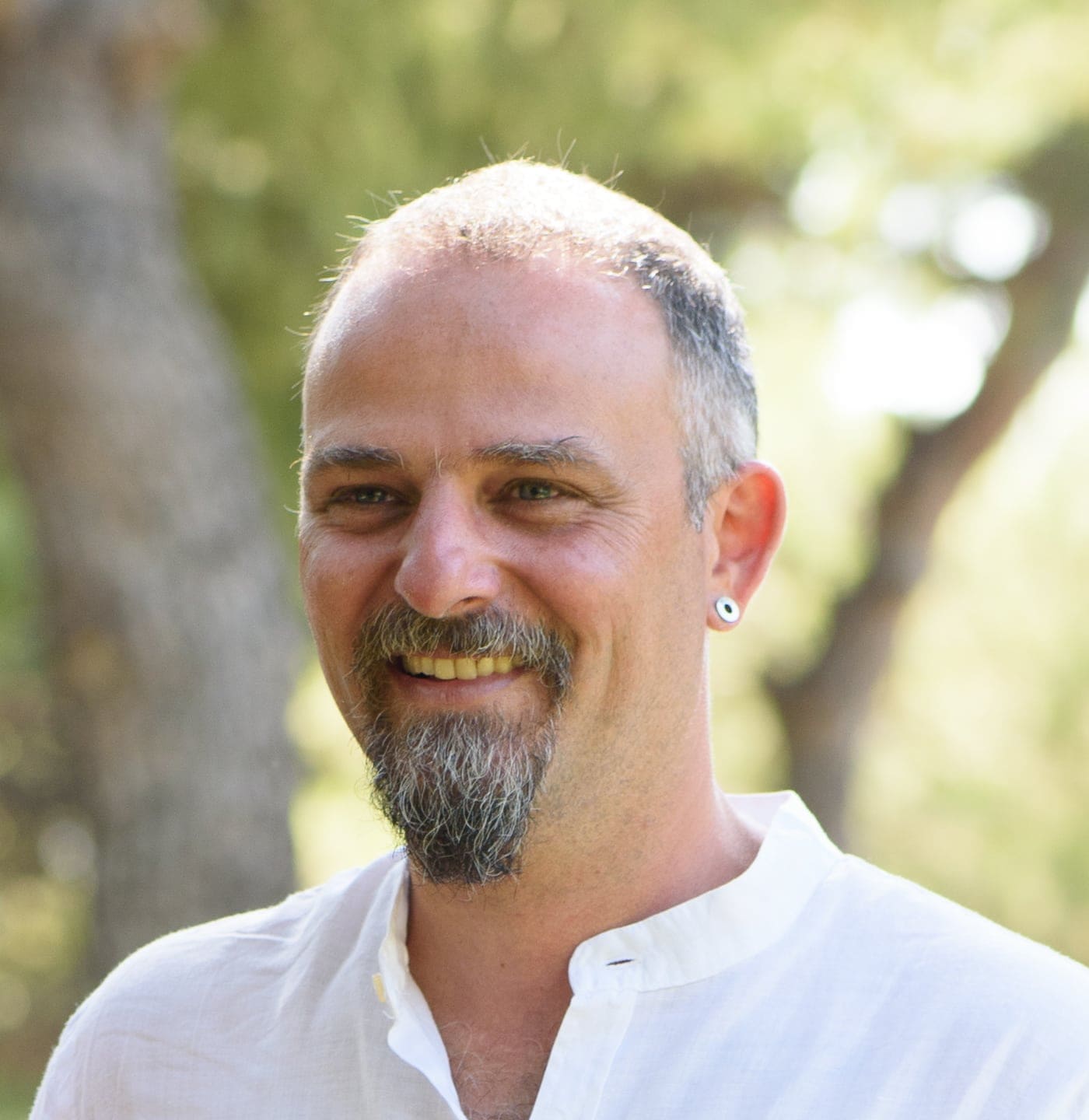 Smiling man with a beard and earrings enjoying the outdoors.